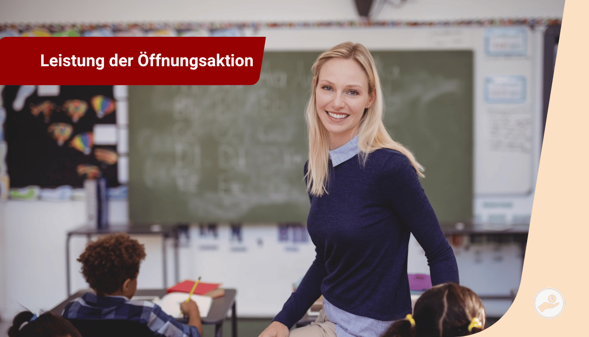 Lehrerin steht lächelnd vor einer Tafel in einem Klassenzimmer, Kinder sitzen an ihren Plätzen.
