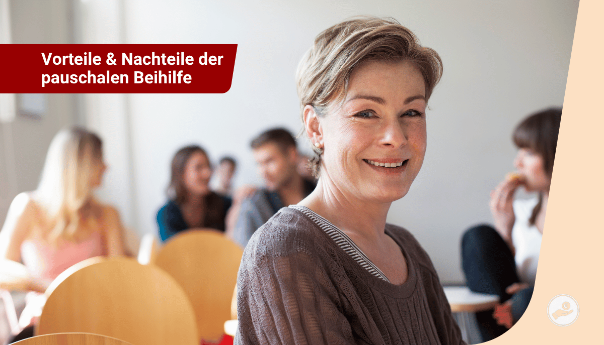 Lehrerin sitzt entspannt im Lehrerzimmer und lächelt in die Kamera, im Hintergrund unterhalten sich weitere Personen.
